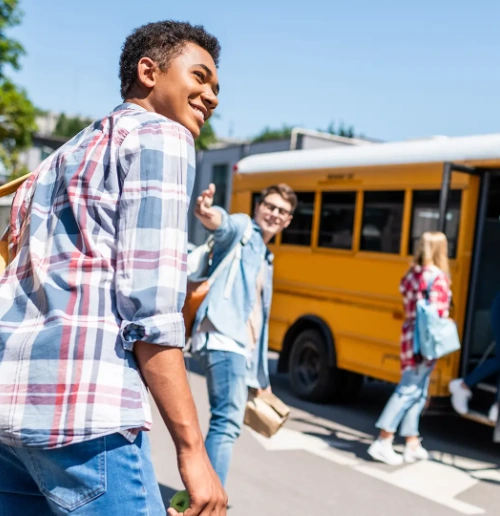 Three students with backpacks walk towards a yellow school bus on a sunny day.