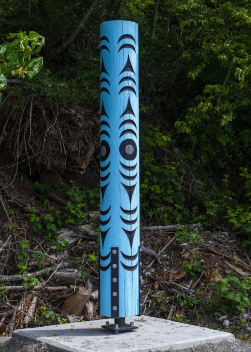 Blue Totem Pole Black Tribal Designs Stands Concrete A blue totem pole with black tribal designs stands on a concrete base outdoors.